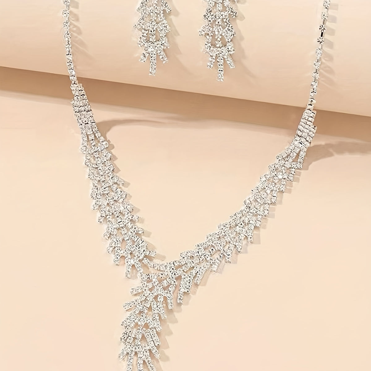 Aveline crystal necklace with V-shaped fringe drop and earrings on a peach background