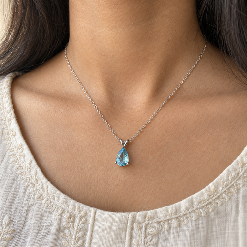 Sky-blue pear-cut pendant on a fine silver-tone chain – worn with an ivory kurta, collarbone view