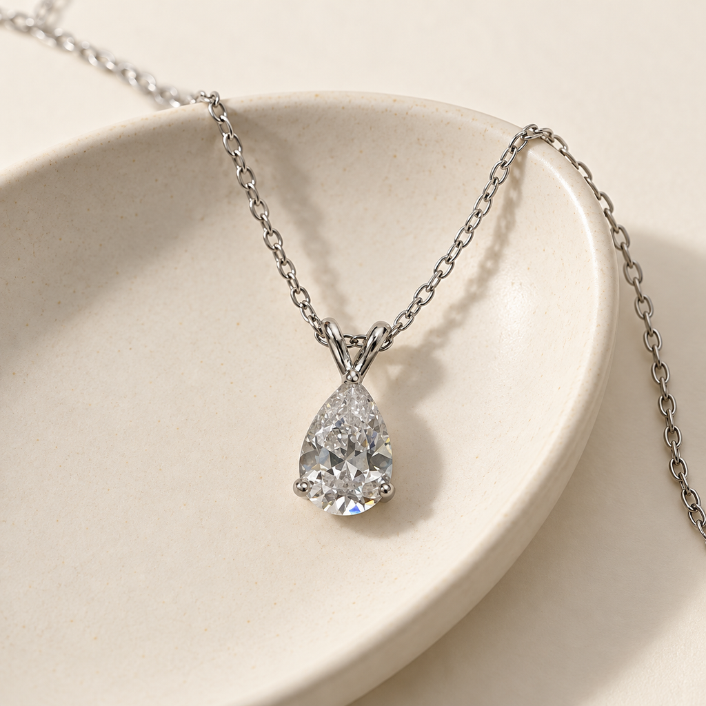 Clear pear-cut pendant on a fine silver-tone chain – on a cream ceramic dish with the chain over the rim