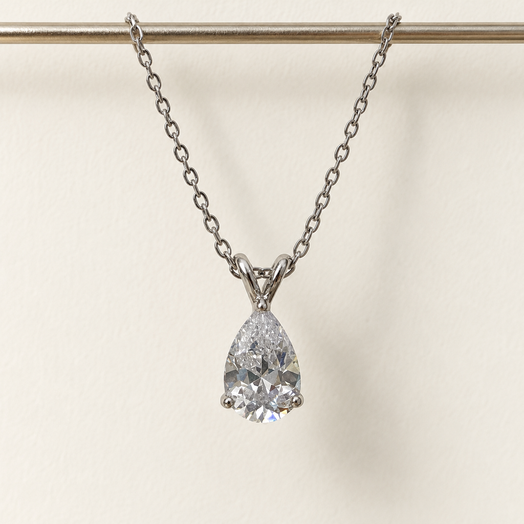 Clear pear-cut pendant on a fine silver-tone chain – hanging straight against an ivory wall
