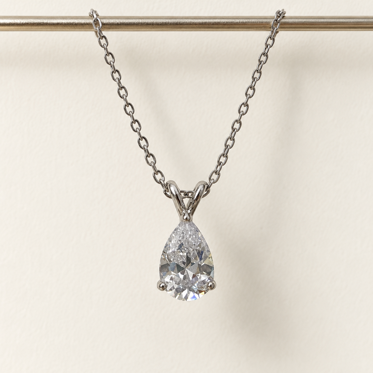 Clear pear-cut pendant on a fine silver-tone chain – hanging straight against an ivory wall