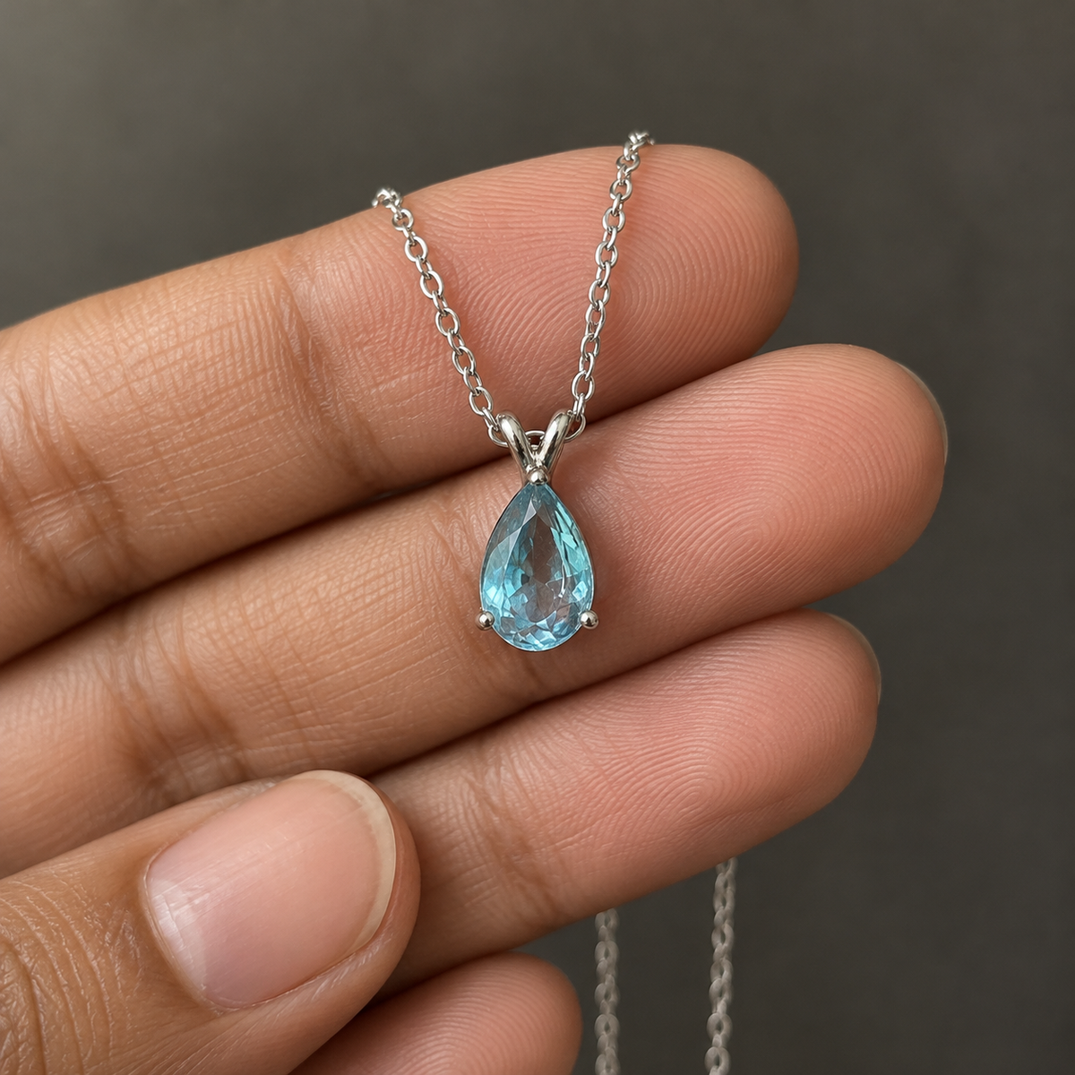 Sky-blue pear-cut pendant on a fine silver-tone chain – held on fingertips with the chain hanging