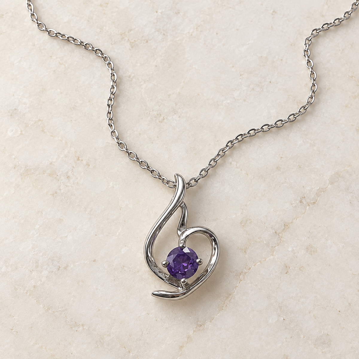 Lumière silver-tone heart pendant with a round violet stone – laid in a curve on an ivory stone surface
