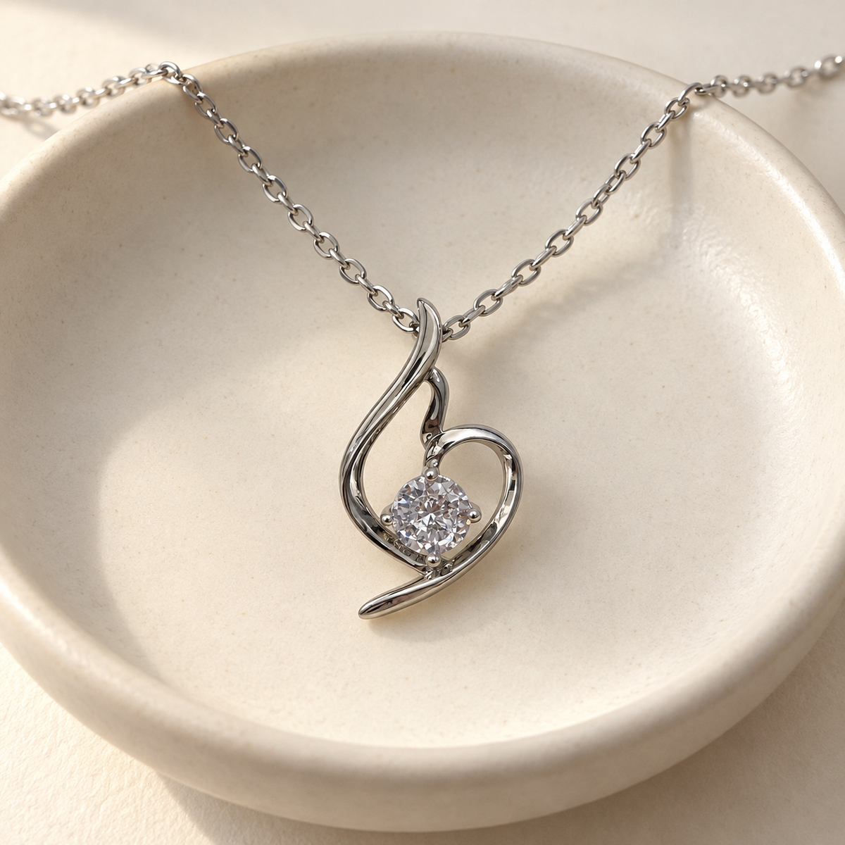 Lumière silver-tone heart pendant with a round clear stone – on a cream ceramic dish with the chain over the rim